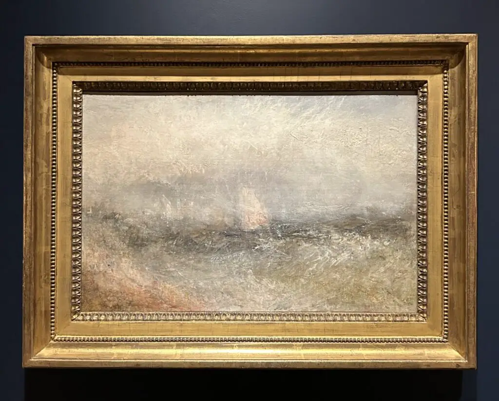 An image of JMW Turner's painting 'Squally Weather' in a gold frame against a dark blue wall.